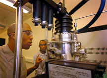 Mechanical engineering doctoral student Baratunde A. Cola, from left, looks through a view port in a plasma-enhanced chemical vapor deposition instrument while postdoctoral research fellow Placidus Amama adjusts settings. The two engineers recently have shown how to grow forests of tiny cylinders called carbon nanotubes onto the surfaces of computer chips to enhance the flow of heat at a critical point where the chips connect to cooling devices called heat sinks. The carpetlike growth of nanotubes has been shown to outperform conventional "thermal interface materials." The research is based at the Birck Nanotechnology Center in Discovery Park at Purdue. (Purdue News Service photo/David Umberger)