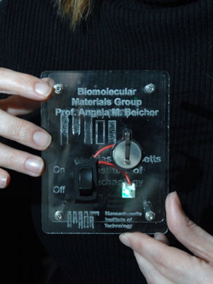 Angela Belcher holds a display of the virus-built battery she helped engineer. The battery -- the silver-colored disc -- is being used to power an LED. 