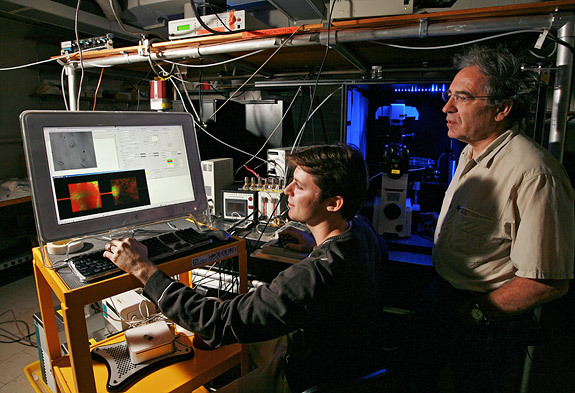 Guillaume Lambert (left), a physics graduate student at Princeton, and Robert Austin, principal investigator of the new Princeton Physical Sciences-Oncology Center and physics professor, observe prostate cancer cells growing on a microhabitat in Jadwin Hall. With their collaborators, the scientists are developing devices and technologies that will allow them to control a wide range of variables in an effort to understand how cancer evolves. The entire experimental setup will be controllable via the Web, enabling their colleagues at peer institutions to conduct experiments remotely. (Photo: Denise Applewhite)
