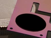 The circular patch of carbon nanotubes on a pink silicon backing is one component of NISTs new cryogenic radiometer, shown with a quarter for scale. Gold coating and metal wiring has yet to be added to the chip. The radiometer will simplify and lower the cost of disseminating measurements of laser power.

Credit: Tomlin/NIST