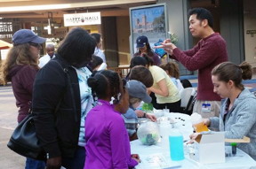 Shaun Mason/UCLA
Jia Chen, education director at the California NanoSystems Institute at UCLA, explains to a crowd of bystanders at the Promenade mall that atoms, while very small, can form large objects in a variety of shapes. Graduate student Pascal Krotee pours out a solution to demonstrate how water can be purified by using a filter made from nanomaterials.