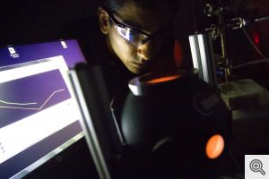 Umar Aslam peers into the light source used during the experiments that revealed how the silver nanocubes captured energy and delivered it to the platinum shells. Image credit: Akhil Kantipuly, Michigan Engineering